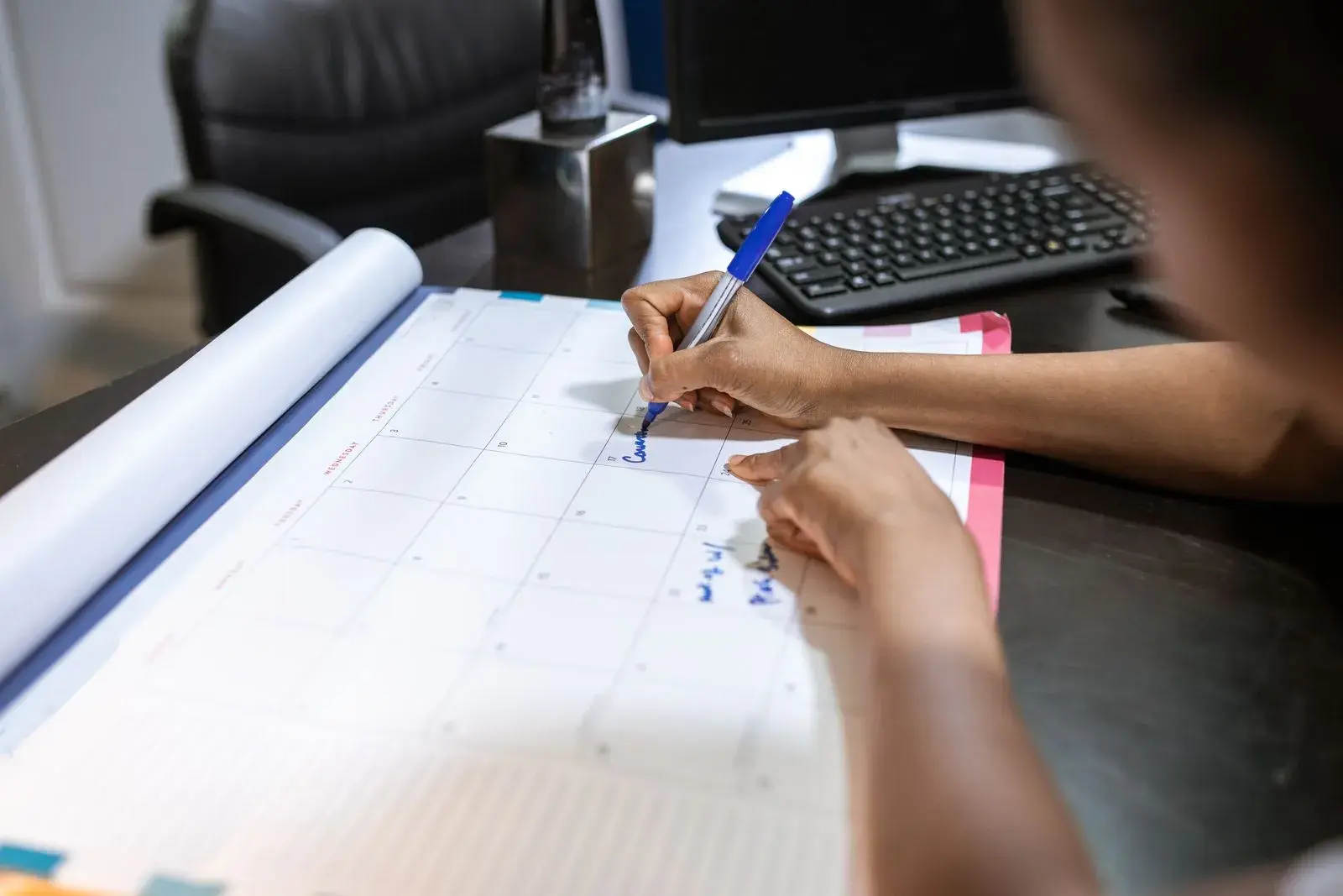 A person writing on a large desk calendar