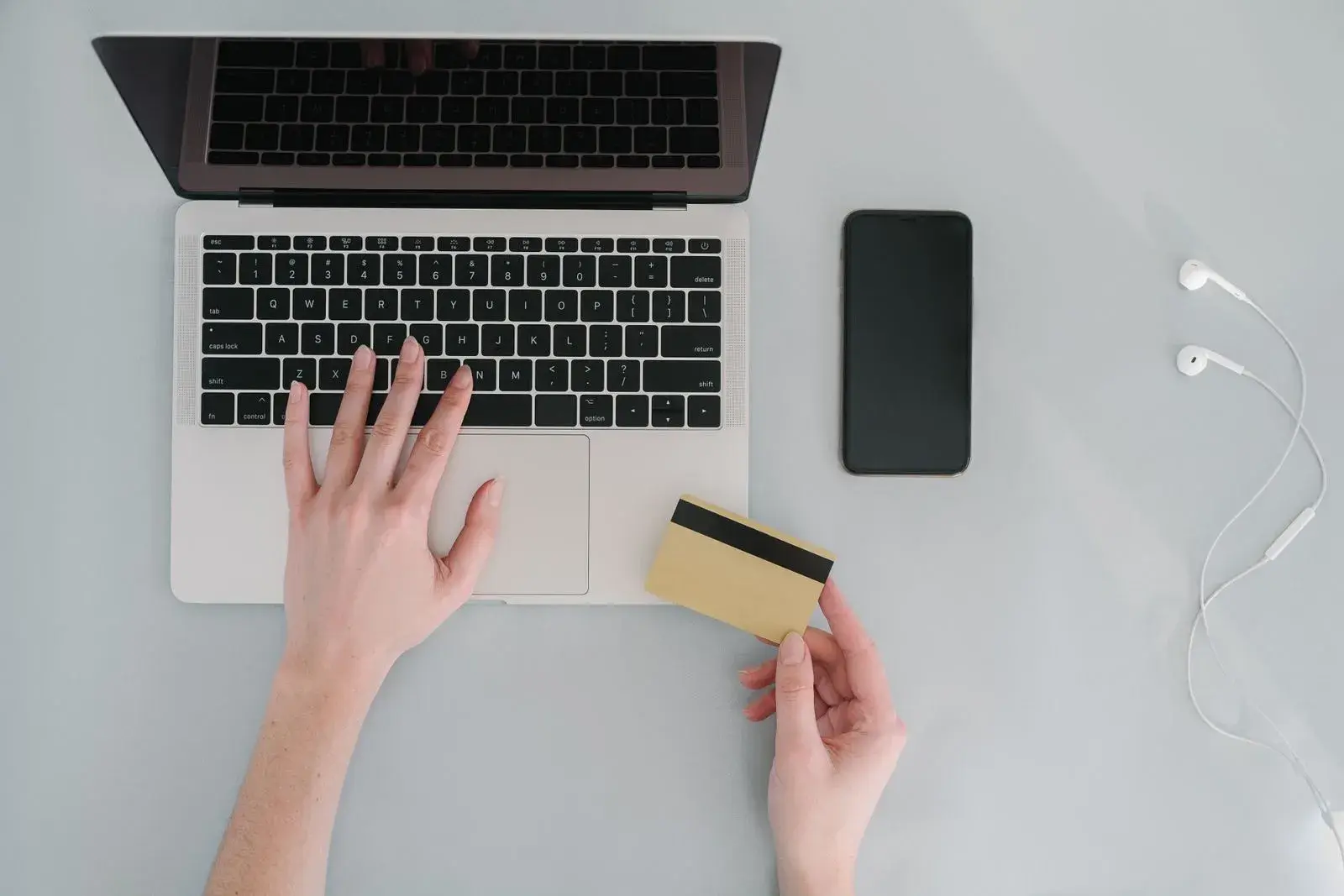 Hands typing on a laptop beside a phone while holding a payment card